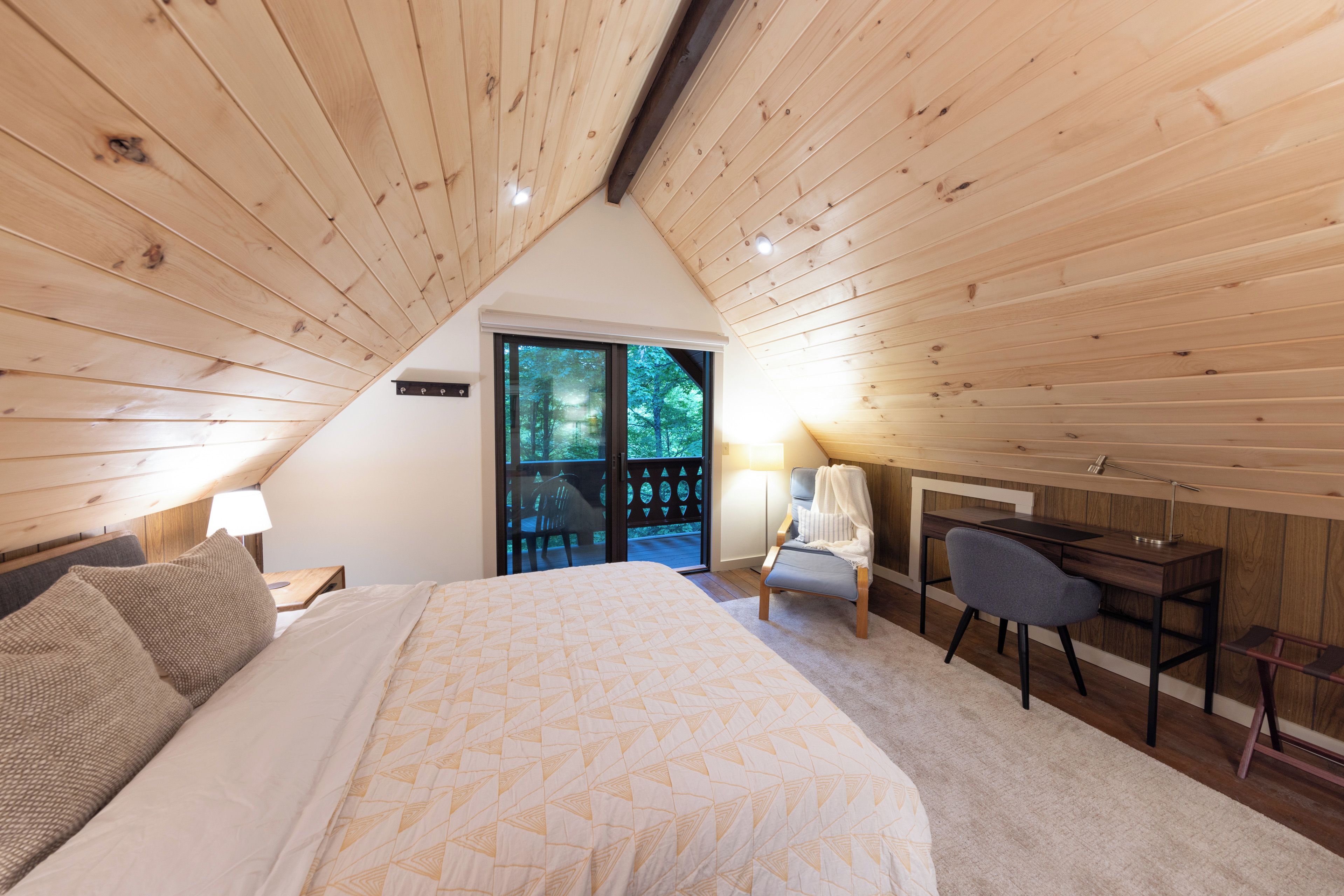 Een slaapkamer met een bed, een bureau en een stoel. Er is een raam met uitzicht op bomen.