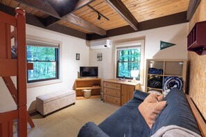 Ein gemütliches Zimmer mit Holzbalkendecke, einer Couch, einem Fernseher und einem Fenster mit Blick auf Bäume.
