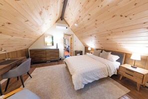 Ein Schlafzimmer mit schrägen Wänden, einem Bett mit weißer Bettdecke, einem Schreibtisch mit Stuhl und einer Kommode.