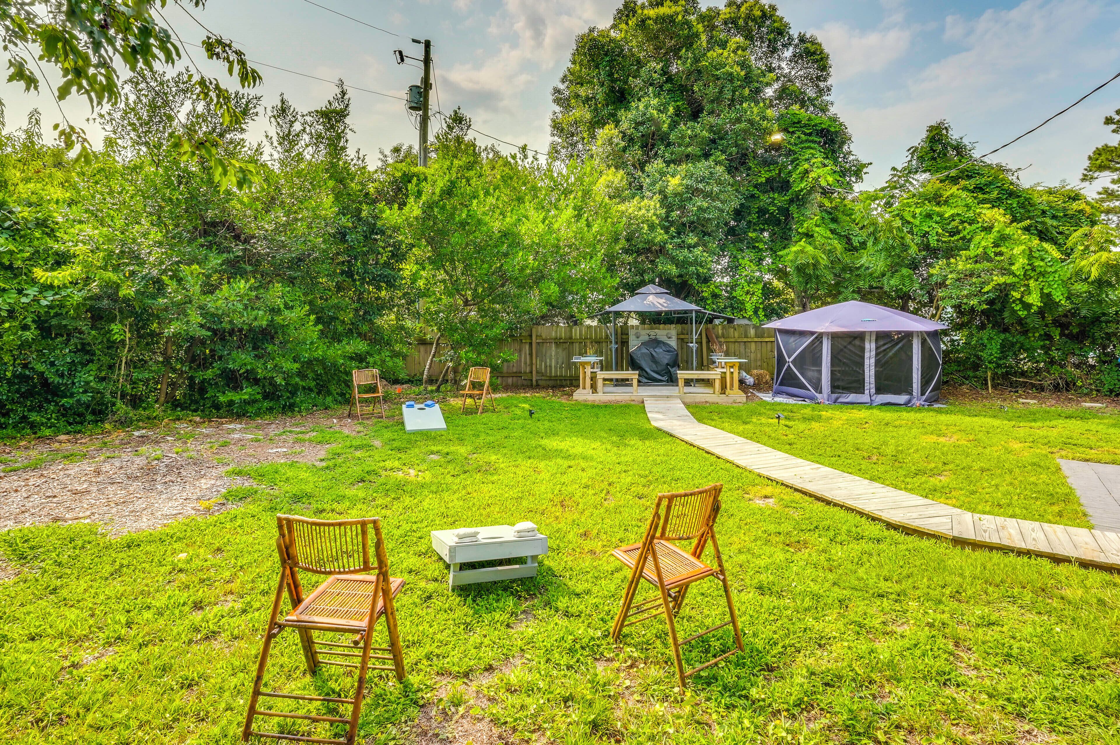 A backyard with a grassy lawn, two wooden chairs, a small table, a barbecue grill, a tent, and a wooden deck.