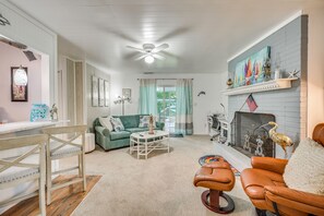 A living room with a green sofa, a coffee table, a fireplace, and a ceiling fan. - Family Beach Retreat w/ Private Pickleball Court (Morehead City)