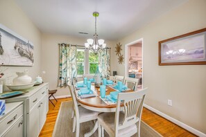 A dining room with a wooden table set for four, white chairs, and a chandelier. - Family Beach Retreat w/ Private Pickleball Court (Morehead City)