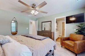 Un dormitorio con cama, ventilador de techo, cómoda, espejo, televisor y planta.