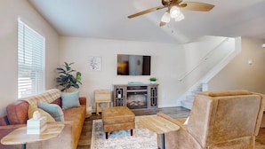 A spacious living room with a sofa, ottoman, and coffee table, a fireplace, and a staircase leading to another level. - Family Home w/ Game Room, Near Lake Hartwell! (Anderson)