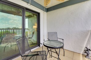 A balcony with a glass door, two mesh chairs, a small round table, and a statue on the floor. - Steps to Sand! Extended Bradenton Beach Getaway (Bradenton Beach)