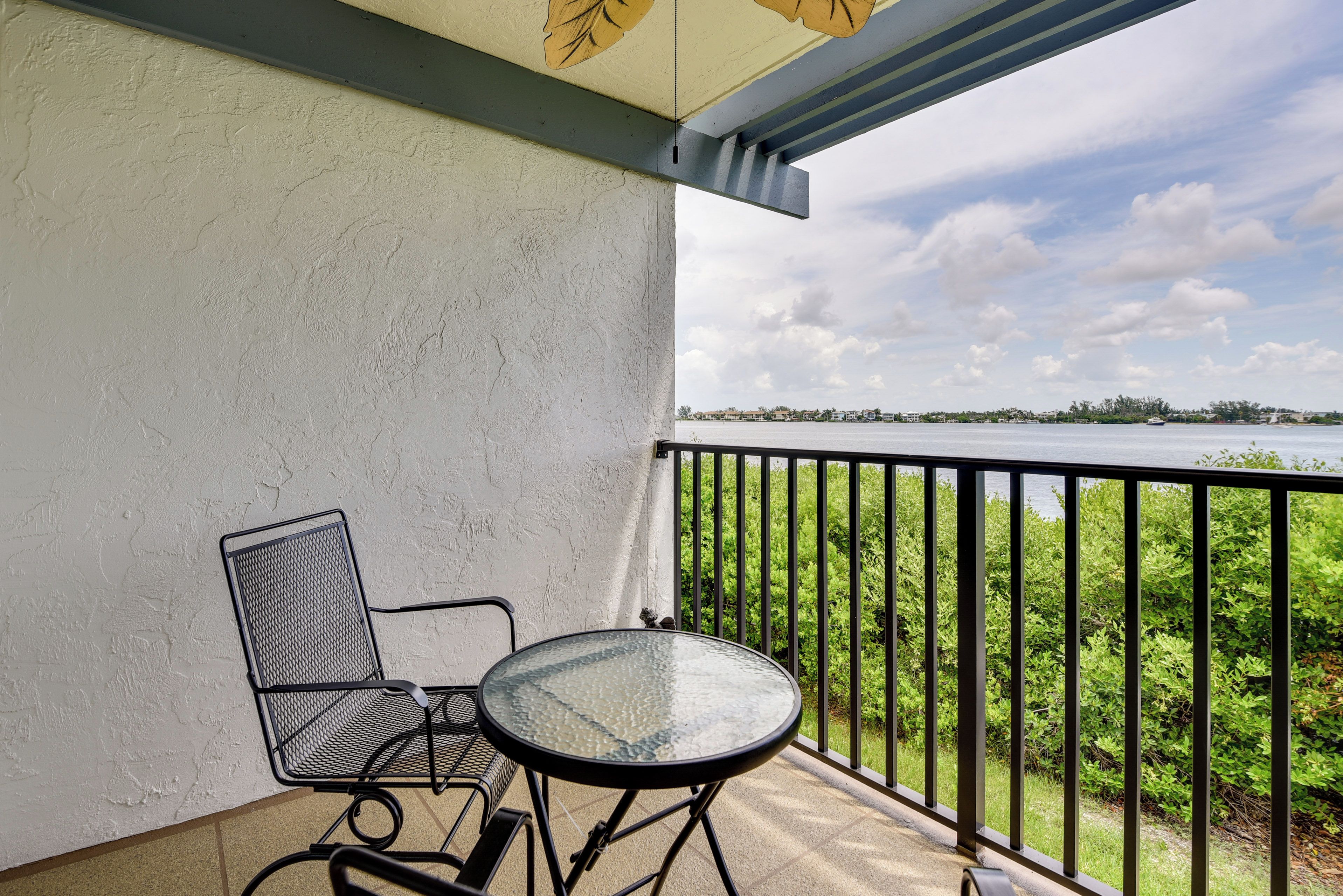 A balcony with a metal chair and table, overlooking a body of water and greenery.