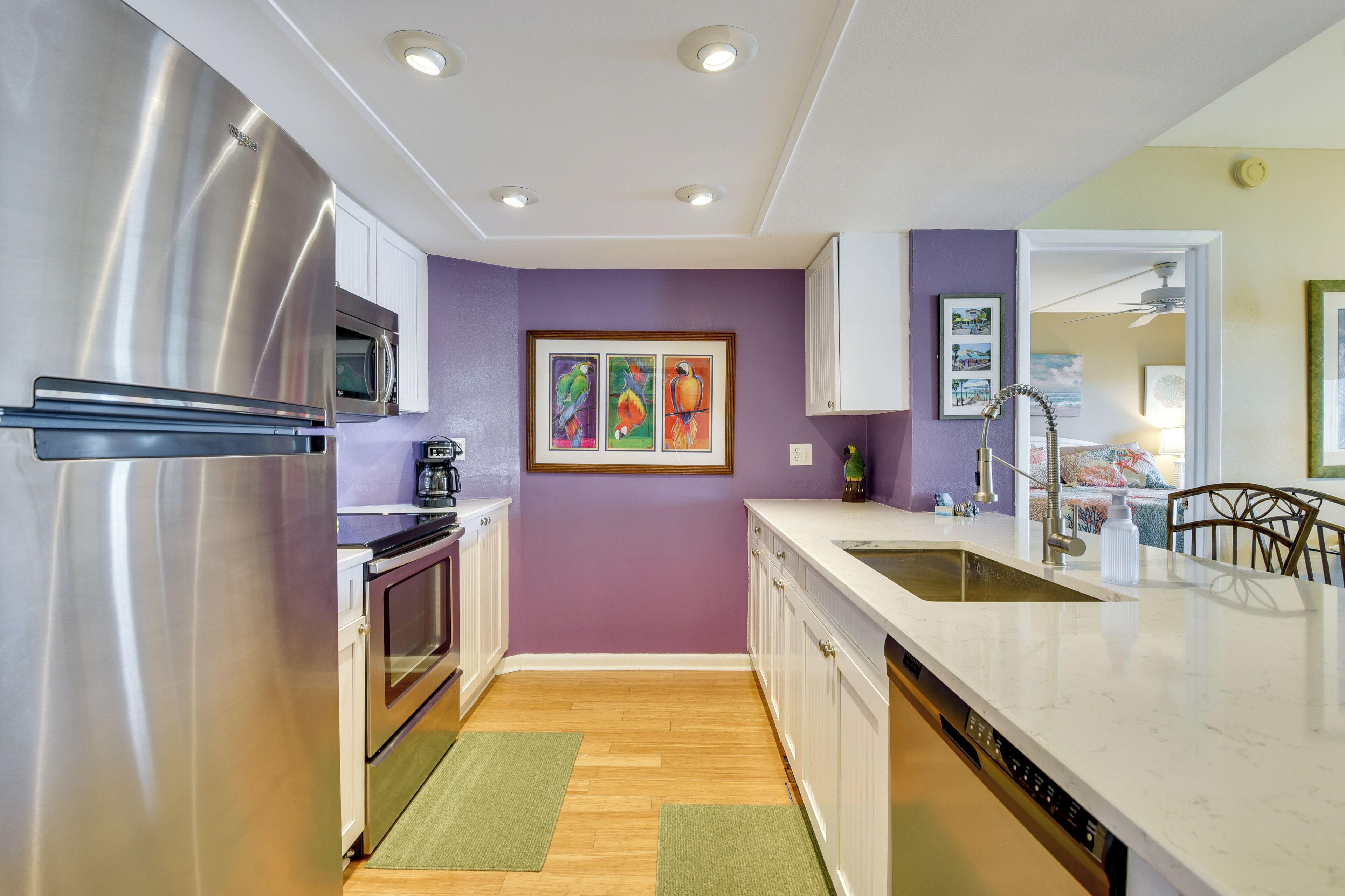 A modern kitchen with stainless steel appliances, a wooden floor, and a purple accent wall.