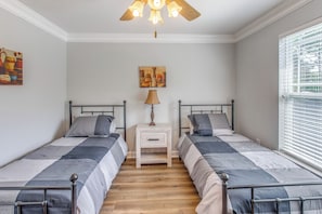 A bedroom with two beds, a nightstand, a lamp, and a painting on the wall. - Golf Days, Pool Vibes! Condo 8 Mi to Sunset Beach (Calabash)