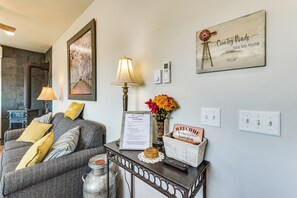 Uma sala de estar aconchegante com lareira, um sofá, uma mesa com abajur, um relógio de parede e uma placa de boas-vindas.