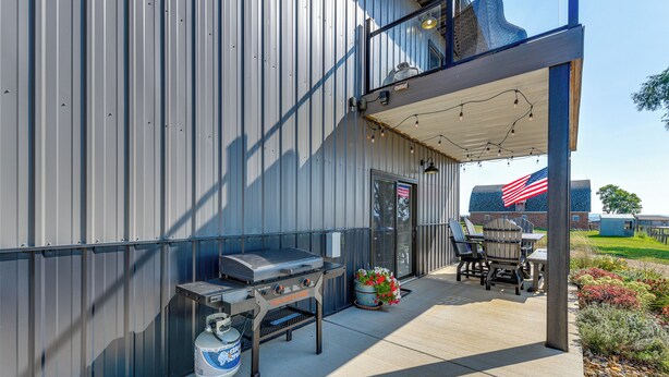 An outdoor patio with a grill, seating, and a view of a building with an American flag.
