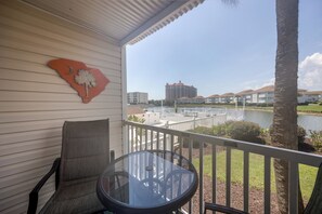 A balcony with a table and chairs, overlooking a body of water with buildings in the background. - Community Pool & Private Patio! N Myrtle Beach Gem (North Myrtle Beach)