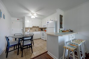 A compact kitchen with white cabinets, a dining table with chairs, a small island with stools, and a ceiling fan. - Community Pool & Private Patio! N Myrtle Beach Gem (North Myrtle Beach)