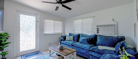 A living room with a blue sofa, a ceiling fan, and a window with blinds.