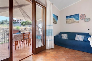 A room with a dining area, a blue sofa, and a view of the outside. - Holiday Home 'Tanit' with Private Terrace, Wi-Fi and Air Conditioning (Villasimius)