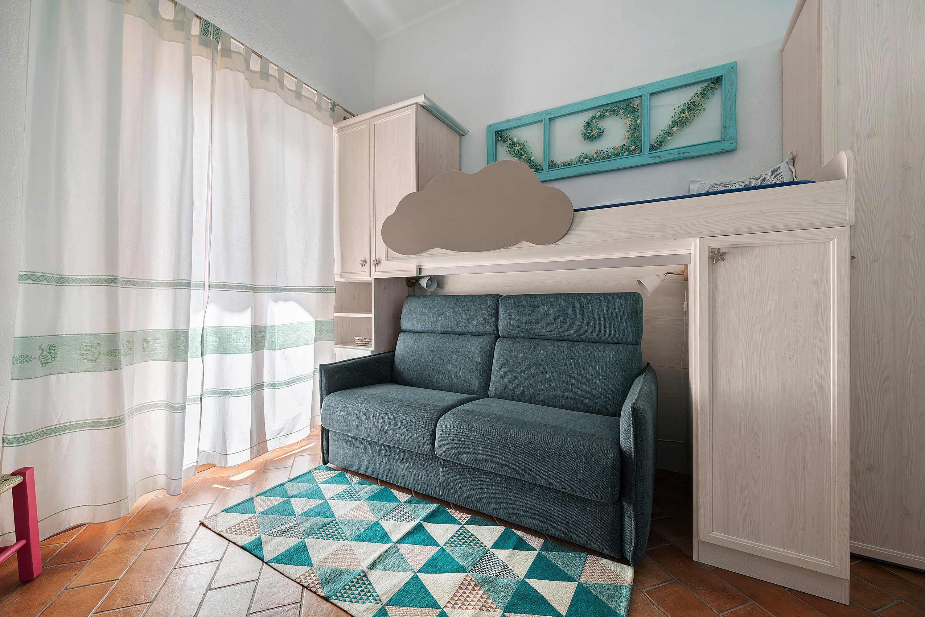 Ein Zimmer mit einem Bett, einem Vorhangfenster, einer Wandablage und einem gemusterten Teppich.