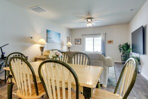 A dining area with a table and chairs, a ceiling fan, a window with curtains, and a television on the wall. - Hammock, Grill & Patio! Sunfish Cove Home (Sunset Beach)