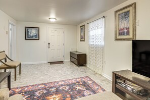 Ein Wohnzimmer mit einem Flachbildfernseher, einem Sofa, einem Couchtisch, einem gemusterten Teppich und einer Tür mit Fußmatte.