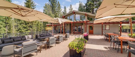 Eine Terrasse im Freien mit Sitzgelegenheiten, Sonnenschirmen und einem Gebäude mit großen Fenstern.