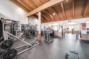 Ein Fitnessraum mit verschiedenen Trainingsgeräten, einer Gewichtbank und einer Decke mit Holzbalken.