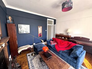 Ein Wohnzimmer mit einem blauen Sofa, einer roten Decke, einem Holztisch und einer Stehlampe.