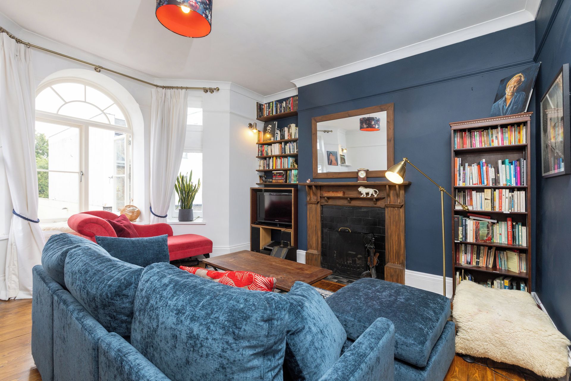 A living room with a fireplace, bookshelves, a red sofa, and a blue armchair.