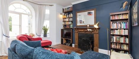 A living room with a fireplace, bookshelves, a red sofa, and a blue armchair.