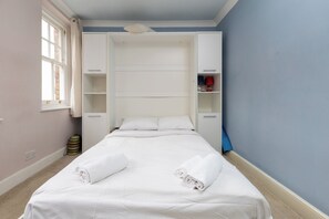 Un dormitori amb un llit, cortines blanques, una finestra i un armari.