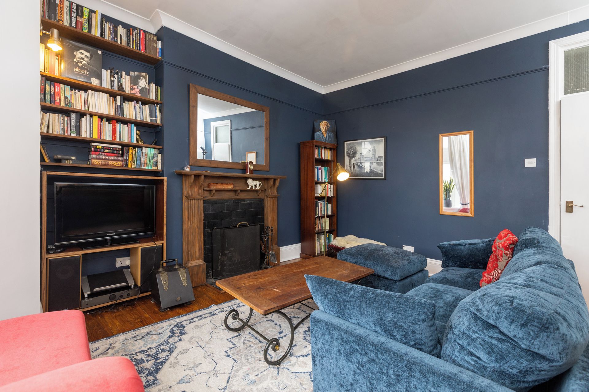 A living room with a fireplace, bookshelves, a television, and a blue sofa.