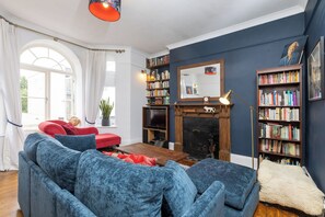 Ein Wohnzimmer mit Kamin, Bücherregalen, einem roten Sofa und einem blauen Sessel.
