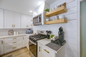 Une cuisine moderne avec des meubles blancs, un four à micro-ondes encastré, une cuisinière et une machine à café.