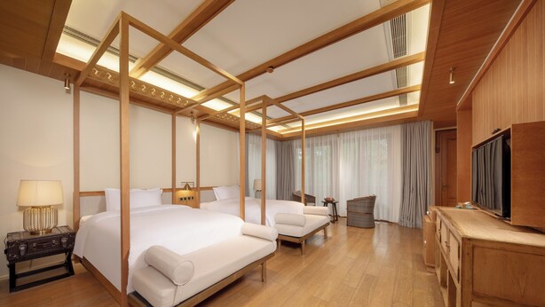 A hotel room with a large bed, a smaller sofa, a desk, and a television.