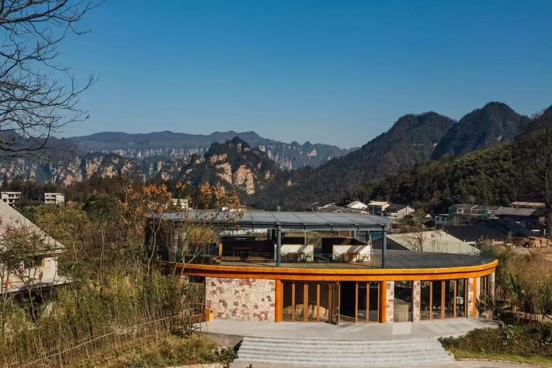 Un bâtiment moderne à la façade incurvée en verre, entouré d’un paysage montagneux.