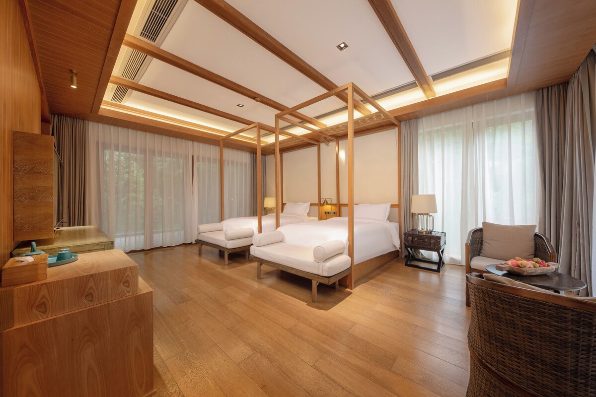 A hotel room with a large bed, two bedside tables, a seating area with a chair, and a wooden floor.
