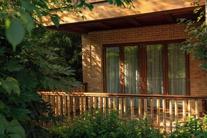Une terrasse en bois avec une rambarde, un mur en briques et une fenêtre donnant sur un paysage verdoyant.