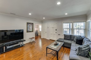 A spacious living room with hardwood flooring, a flat-screen TV, a grey sofa, and a glass coffee table. - Walk to Metro! Historic View Park Home w/ Patio (Los Angeles)