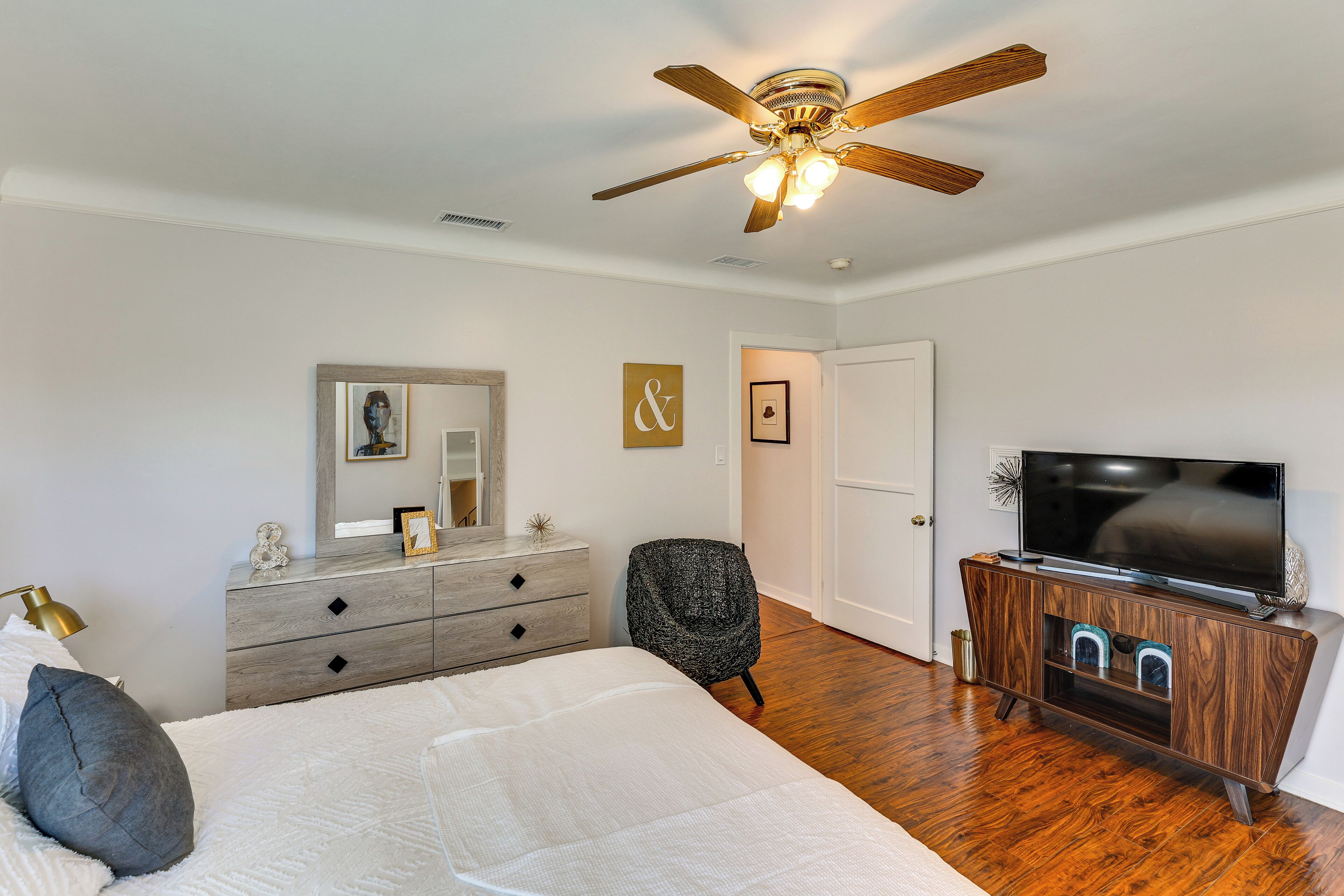 A bedroom with a bed, a dresser, a chair, a television, and a ceiling fan.
