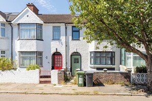 A two-story house with a red door, a bay window, and a brick wall. - Light Filled First Floor Studio with Bay Window (Greater London)