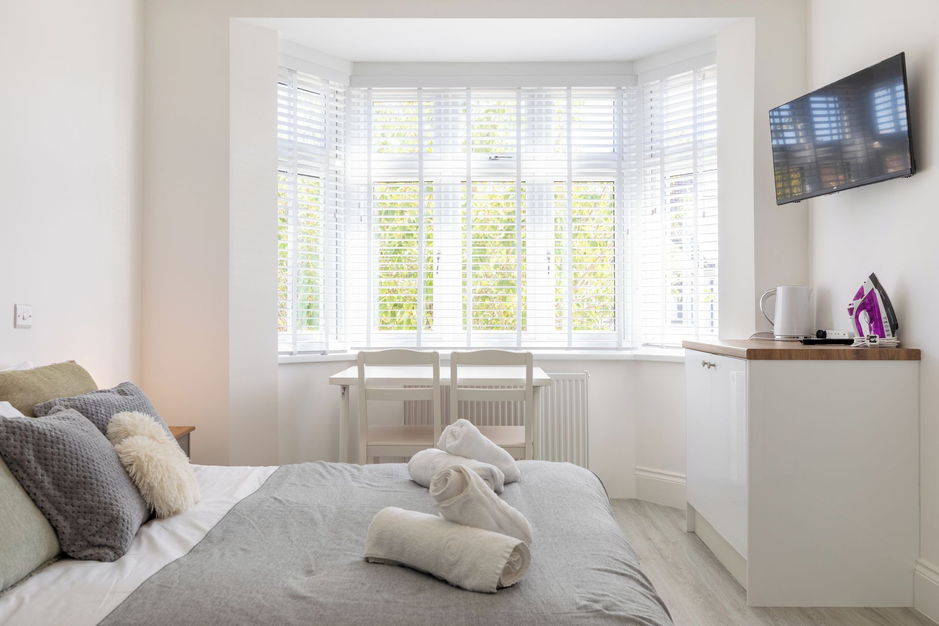 Een slaapkamer met een bed, een bureau en een aan de muur bevestigde televisie.