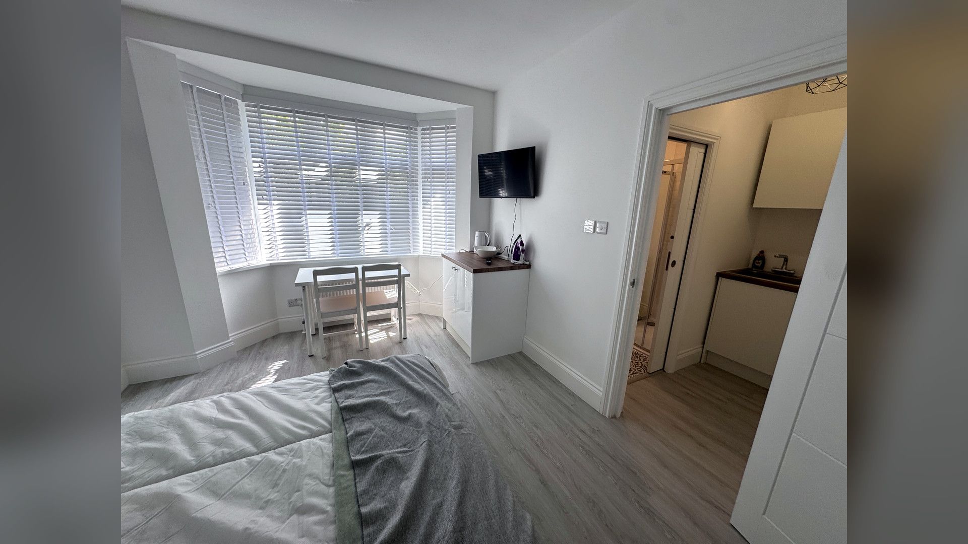 A compact bedroom with a bed, a desk, and a TV mounted on the wall.