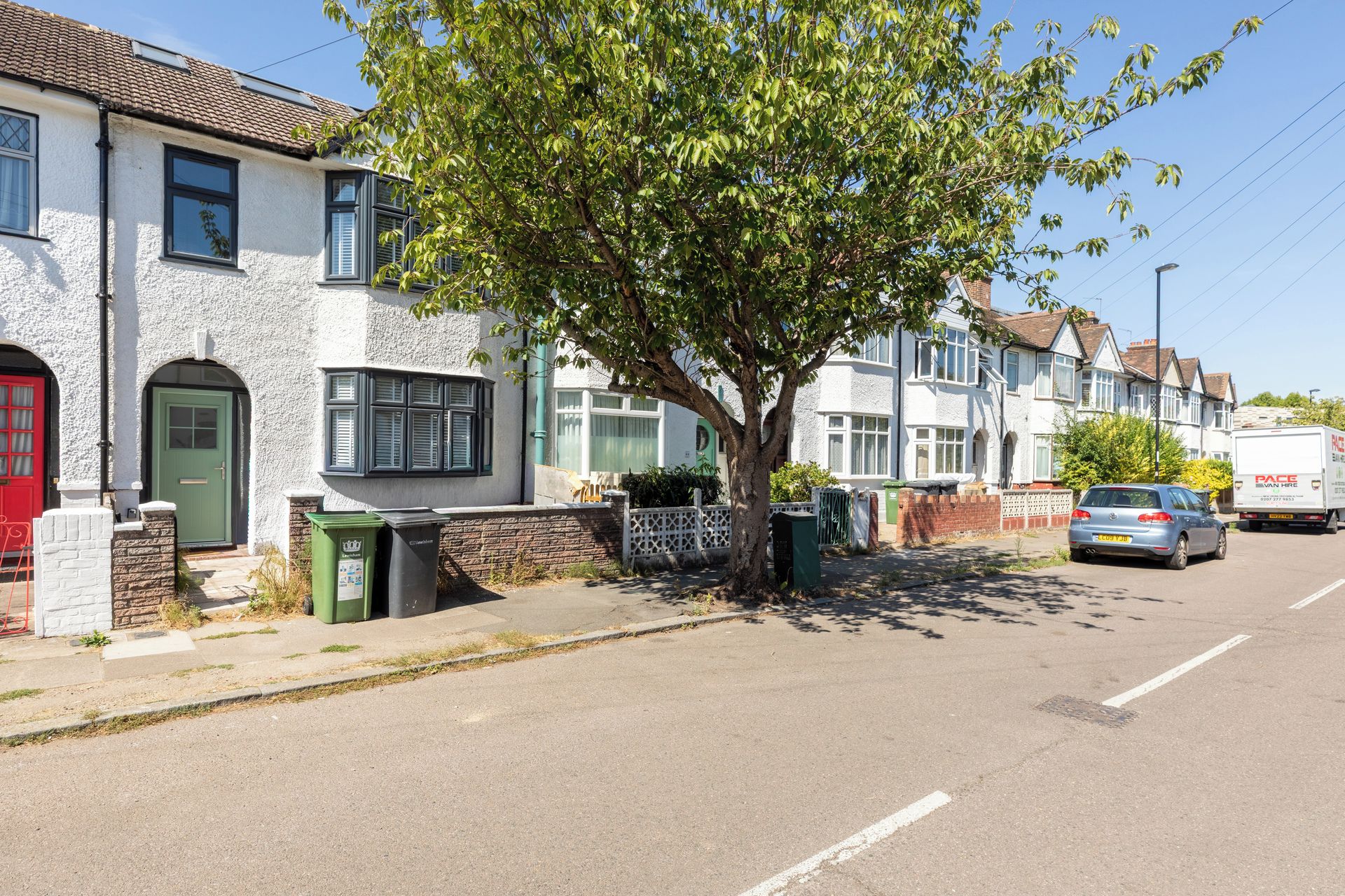 Una calle residencial con casas, un árbol y coches aparcados.
