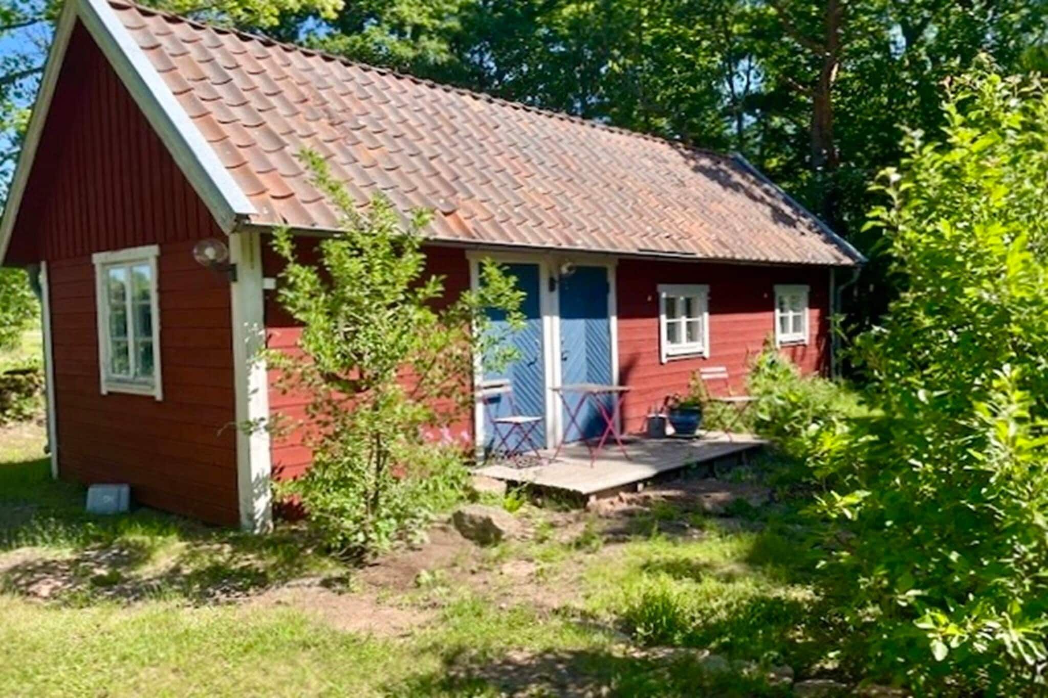 Une petite maison en bois rouge, avec un toit en tuiles, un porche à l’avant et un petit jardin.