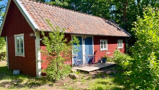 Pieni punainen puutalo, jossa on tiilikatto, kuisti ja pieni puutarha.