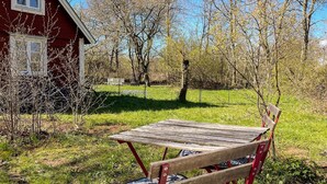 Tunnelmallinen ulkoalue, jossa on puinen pöytä ja penkki, ja jota ympäröi nurmikko ja puut.