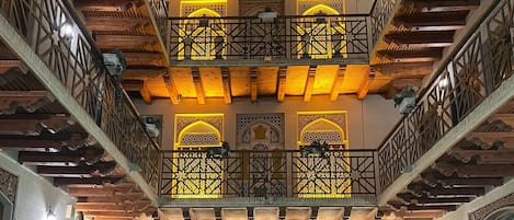 Un atrio de varios niveles con balcones de madera, una fuente central y decoración tradicional.