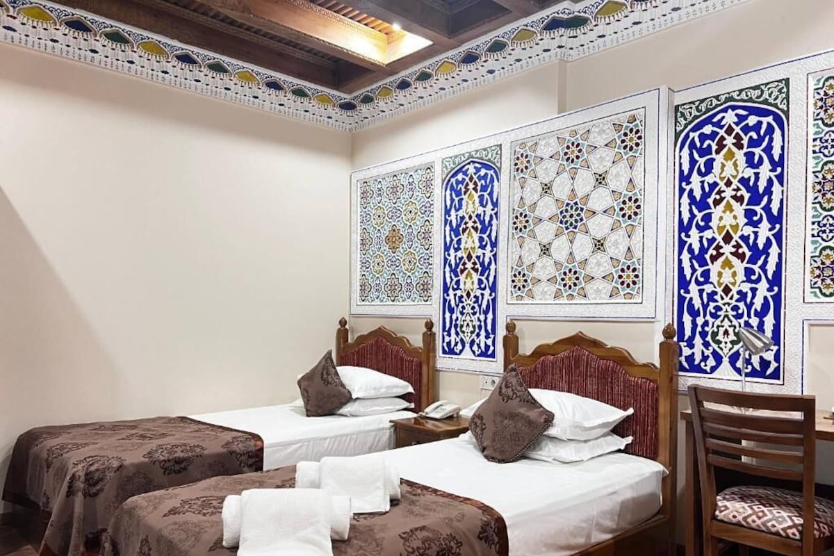 A hotel room with two beds, a wooden chair, and decorative wall panels.