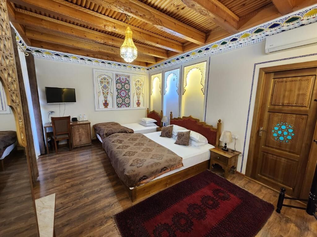 A bedroom with a wooden ceiling, a bed with a patterned bedspread, a nightstand with a lamp, and a door with a decorative panel.