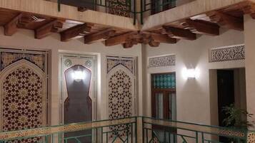 A multi-level interior with ornate architectural details, including a balcony with green railings and a tiled floor.