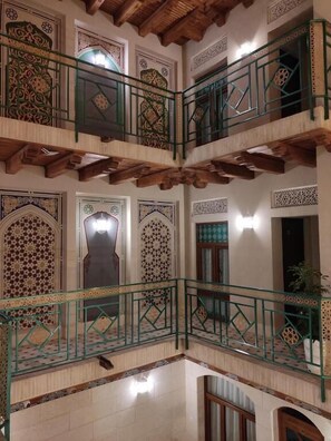 Un interior de varios niveles con detalles arquitectónicos ornamentales, incluyendo un balcón con barandillas verdes y un suelo de baldosas.