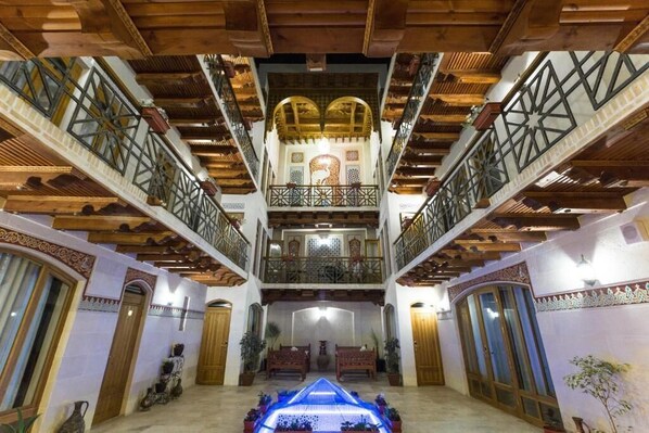 Un interior espacioso con una fuente central, vigas de madera y balcones ornamentales.