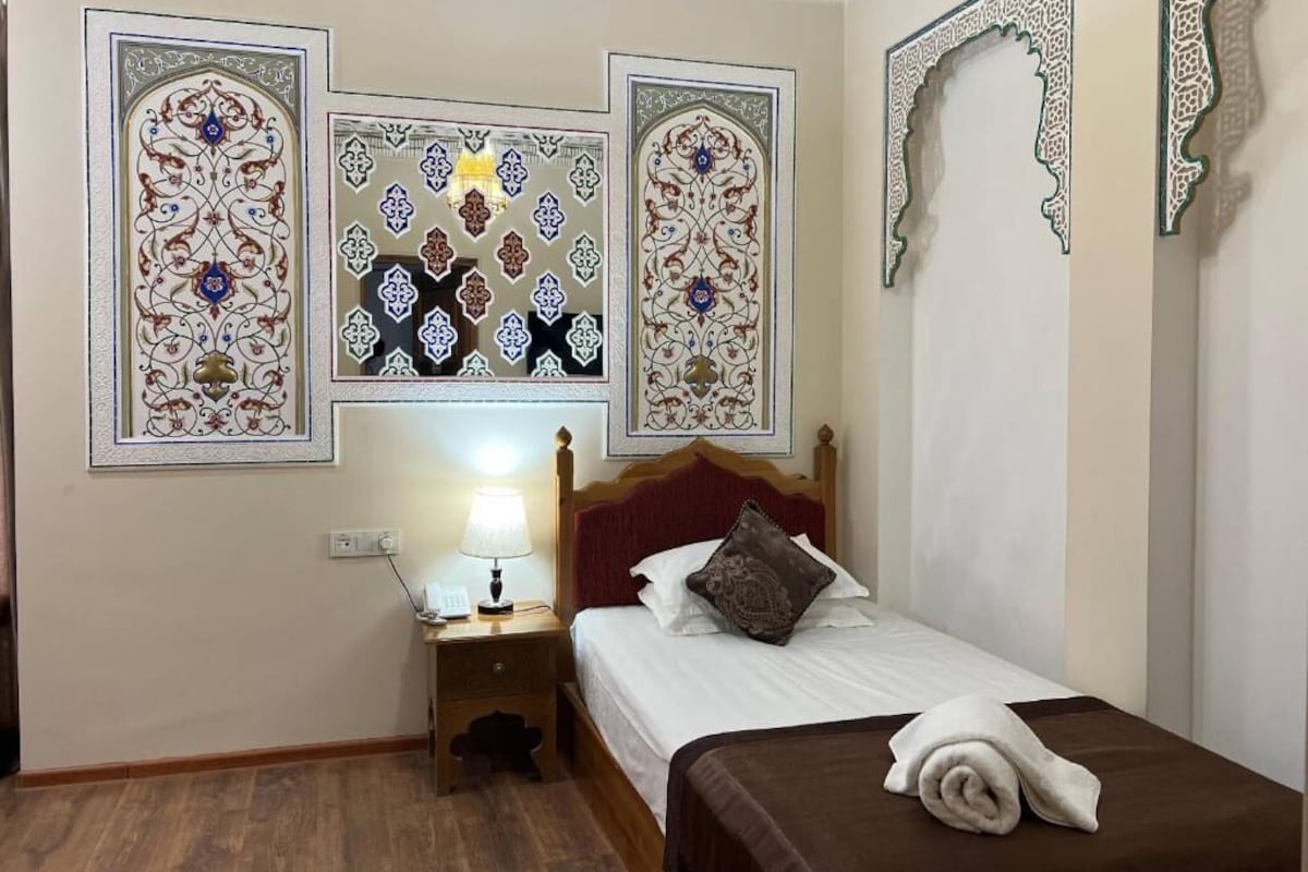 A hotel room with a bed, nightstand, lamp, and decorative wall panels.